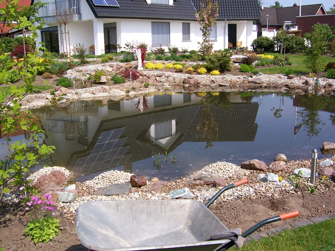 Gartenteich vor einem Wohnhaus nach der Reinigung, Schubkarre im Vordergrund